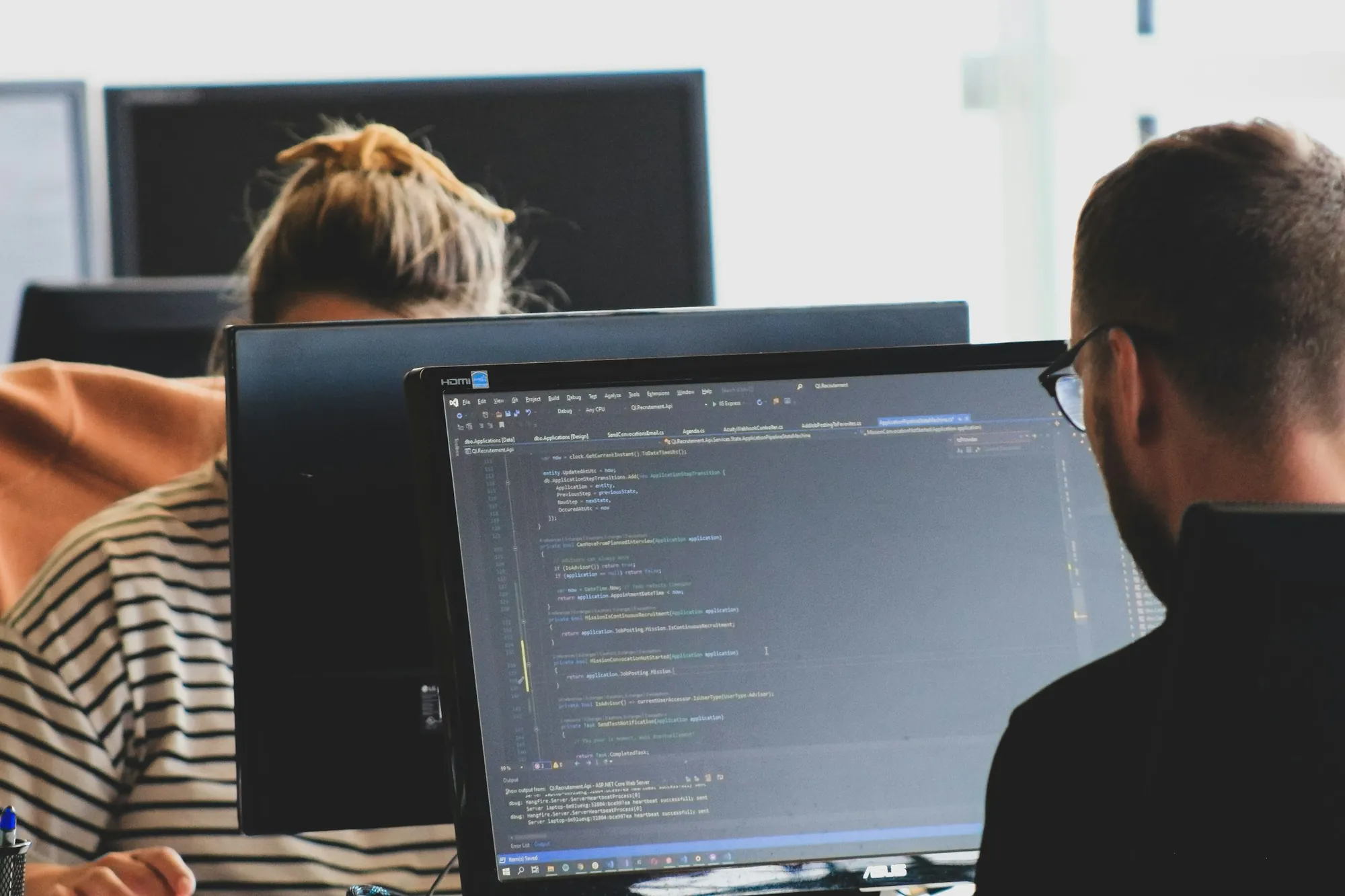 Two developers working on code across several monitors