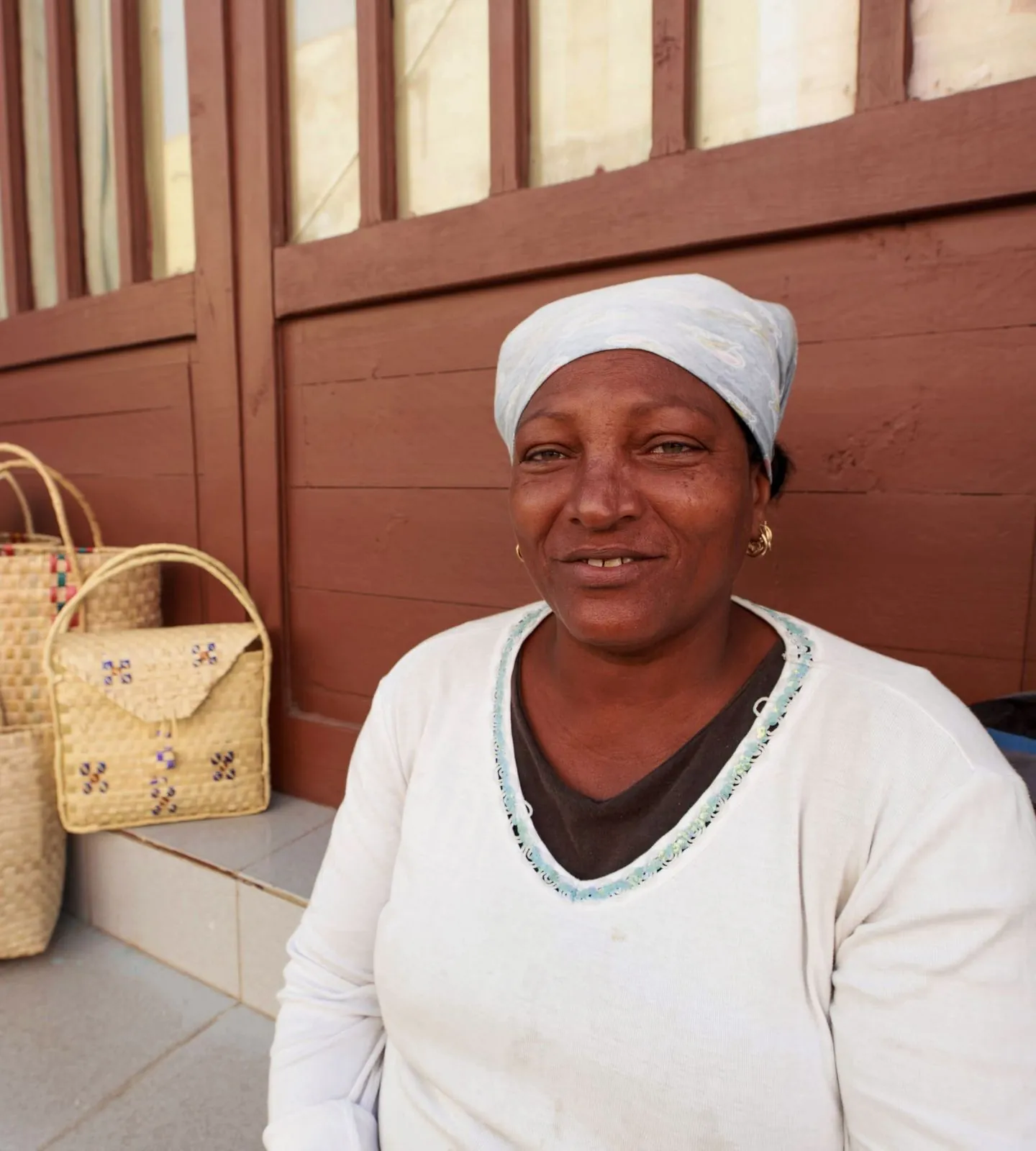 A shopkeeper smiles beside her stall of woven straw bags and hats